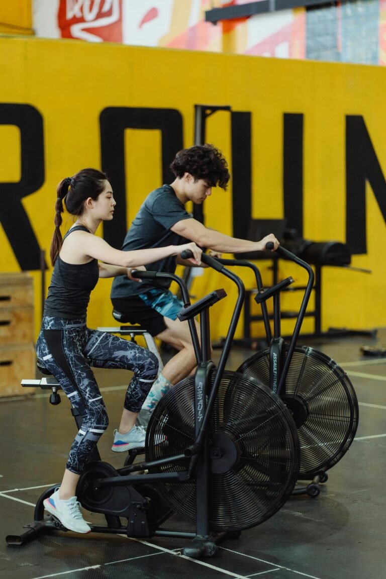 Asian couple in activewear working out on stationary bikes indoors, promoting fitness.