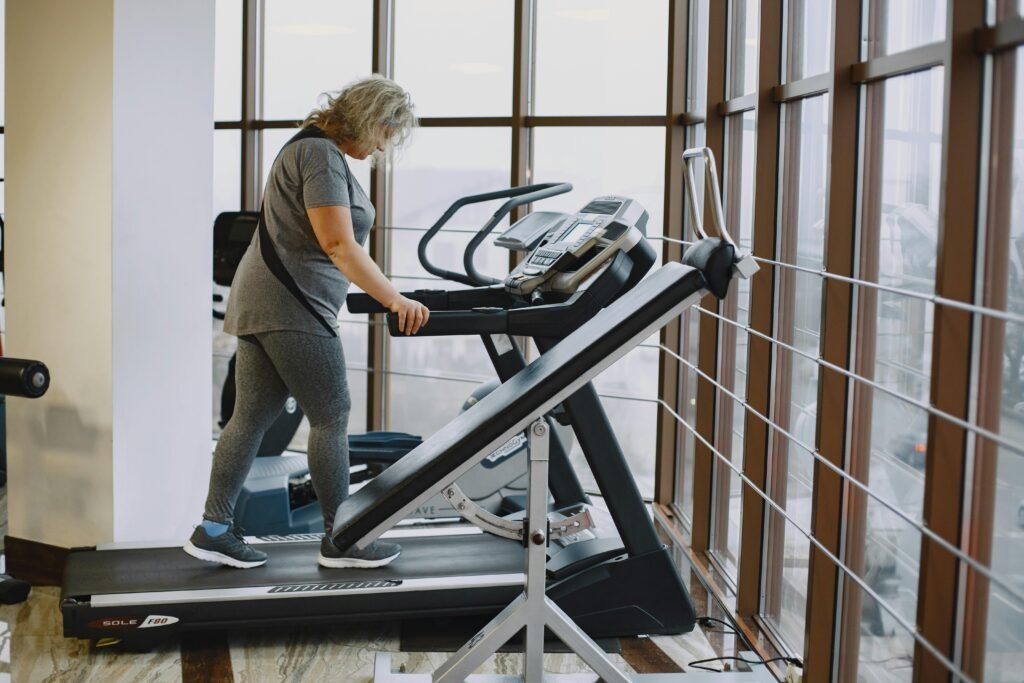 Adult woman exercising on a treadmill in a bright, modern gym setting.