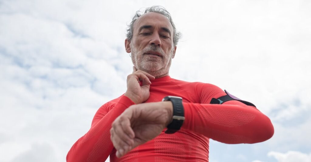 Elderly man in red active wear checking wristwatch outdoors under cloudy sky.